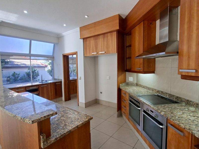 Spacious kitchen featuring granite countertops, ample wooden cabinetry, built-in double oven, electric hob, and a breakfast bar island.
