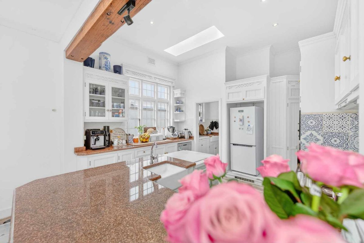 A bright and well-appointed kitchen featuring granite countertops, a farmhouse sink, exposed timber beam, and a skylight, with ample built-in cabinetry.
