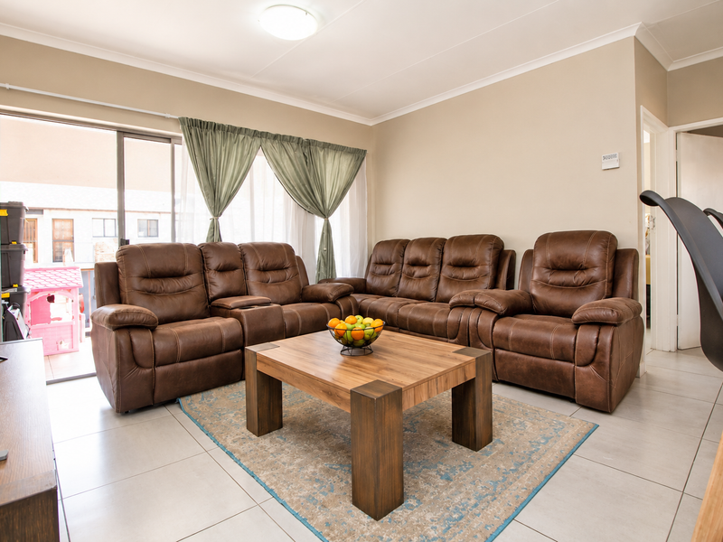 A well-lit living room featuring neutral tiled flooring, cove cornicing, and a large sliding glass door providing access to the outdoor area.