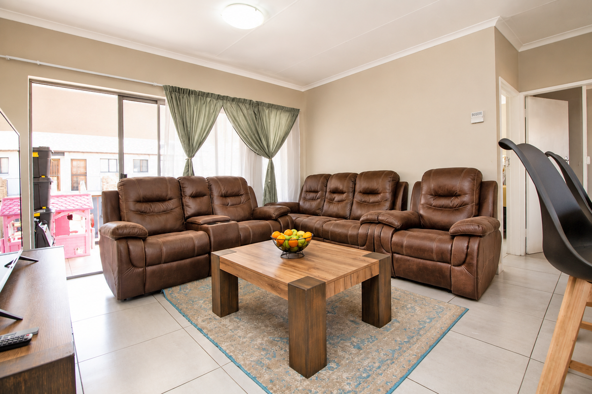A well-lit living room featuring neutral tiled flooring, cove cornicing, and a large sliding glass door providing access to the outdoor area.