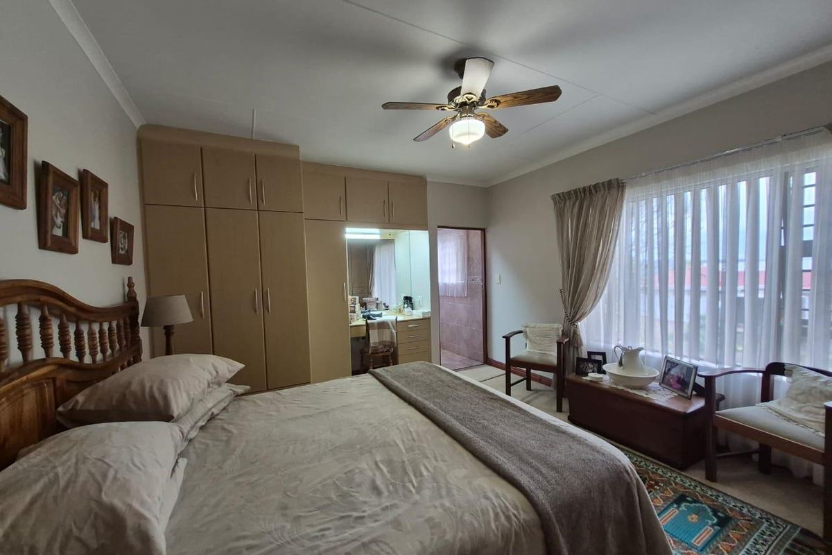 A spacious bedroom featuring built-in cupboards with an integrated vanity area, a ceiling fan, and large windows allowing for natural light.