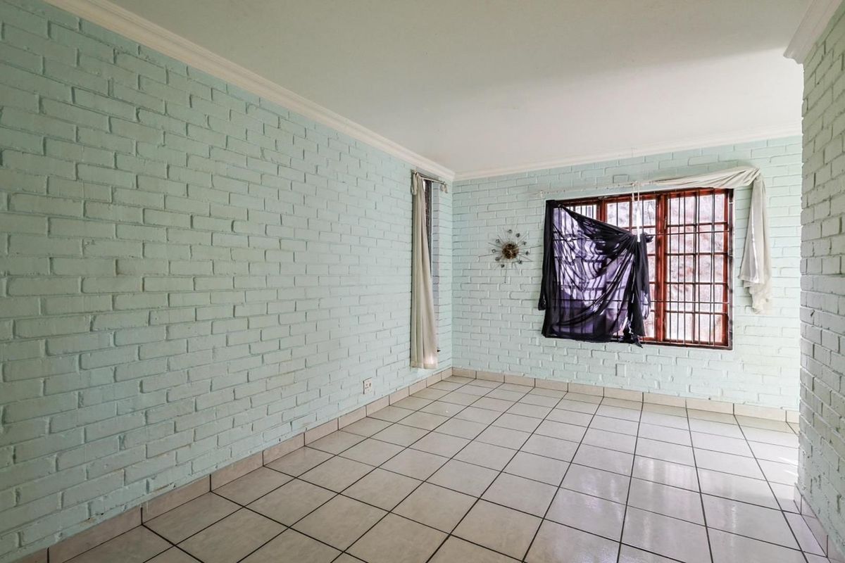 An empty room featuring light blue painted brick walls, white ceramic floor tiles, and a window fitted with security bars.