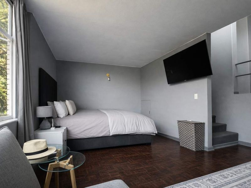 A well-maintained bedroom featuring dark parquet flooring, neutral grey walls, and a built-in staircase leading to an upper level.