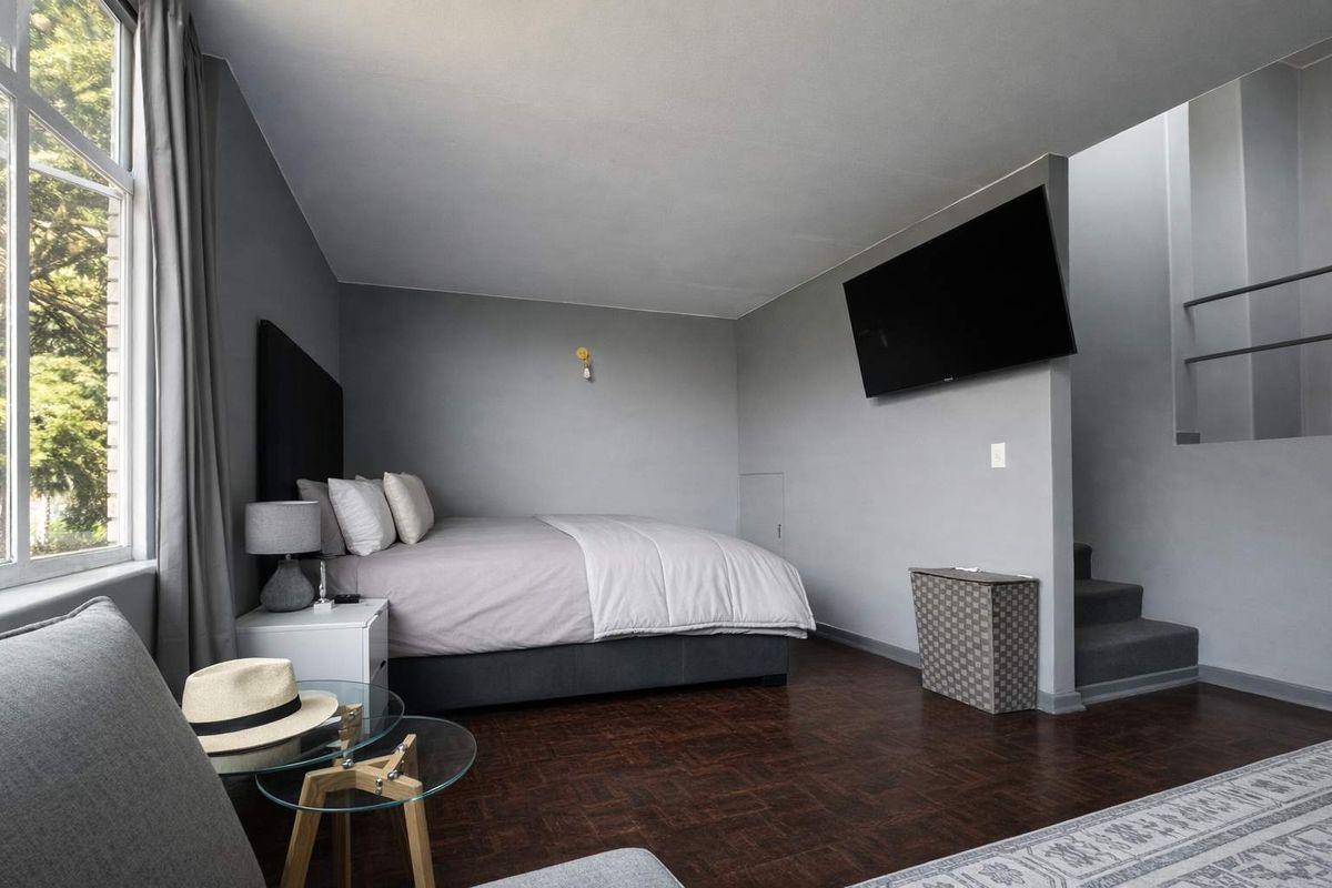 A well-maintained bedroom featuring dark parquet flooring, neutral grey walls, and a built-in staircase leading to an upper level.