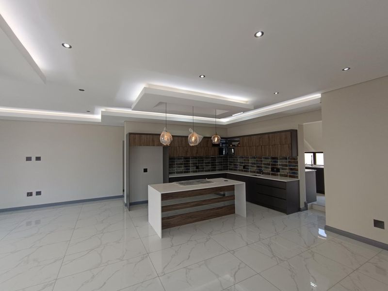 Modern open-plan kitchen featuring a central island, sleek built-in cabinetry, stone countertops, and elegant recessed ceiling lighting with marble-look tiled flooring.