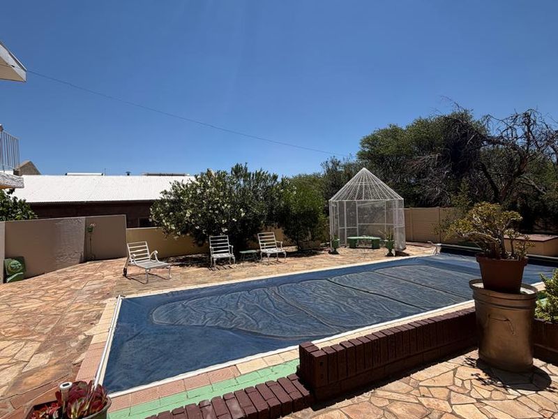 Outdoor pool area featuring a swimming pool with a cover, surrounded by stone paving and a brick retaining wall.