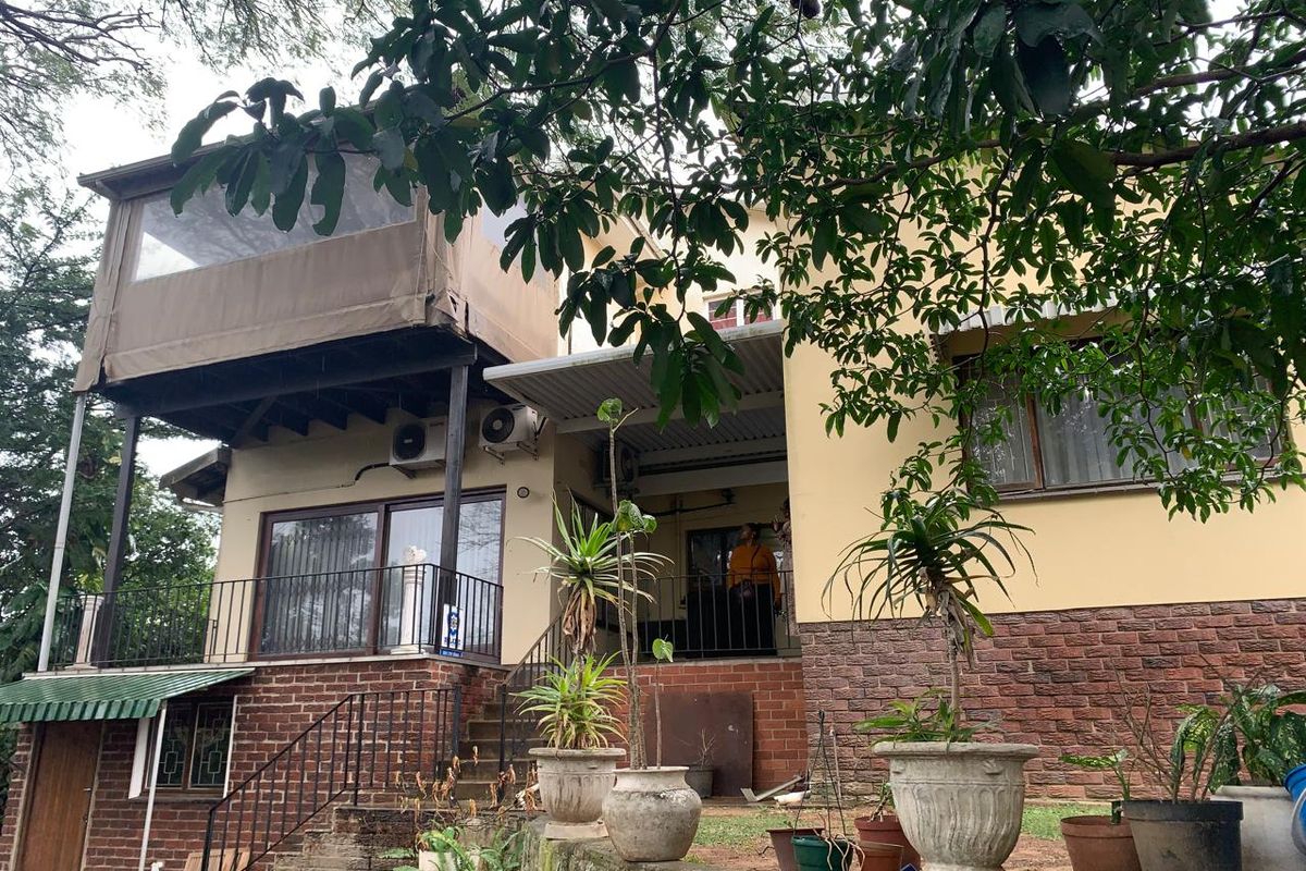 Rear elevation of the house featuring a raised patio with canvas enclosure, brick cladding, and external air conditioning units.
