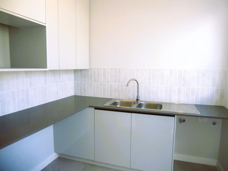 A clean, modern laundry area featuring built-in cabinetry, a stone benchtop, and a stainless steel double sink with a tiled splashback.