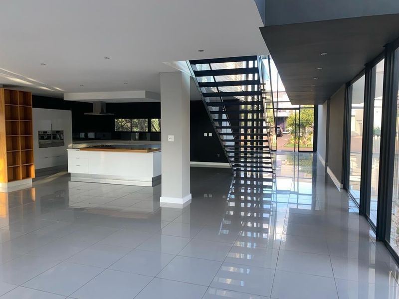 Spacious open-plan living area featuring a modern kitchen with island, sleek tiled flooring, and a striking architectural staircase with floor-to-ceiling glass windows.