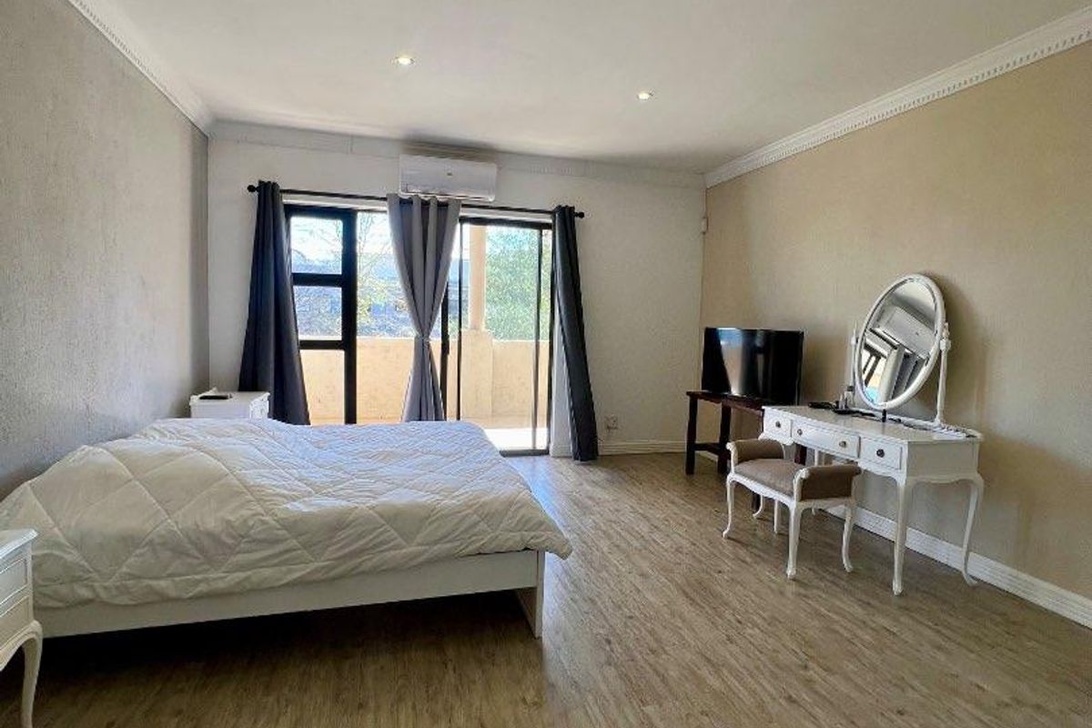 Spacious bedroom featuring wood-look laminate flooring, recessed ceiling lighting, crown molding, and sliding glass doors leading to a private balcony.