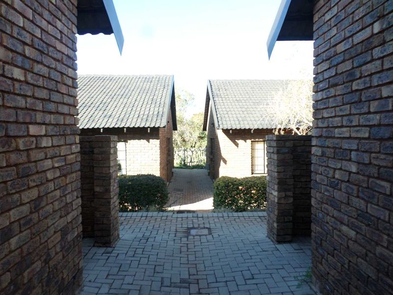 A view of the exterior rear area featuring face brick construction, tiled roofing, and a paved walkway between two residential units.