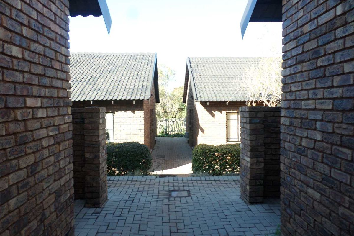 A view of the exterior rear area featuring face brick construction, tiled roofing, and a paved walkway between two residential units.