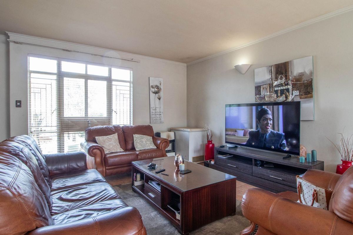 A comfortable living room featuring tiled flooring, large windows with security bars, and wall-mounted lighting fixtures.