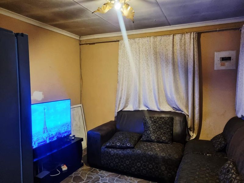 A living room area featuring tiled flooring and an electrical distribution board, currently showing significant signs of wear and ceiling damage.