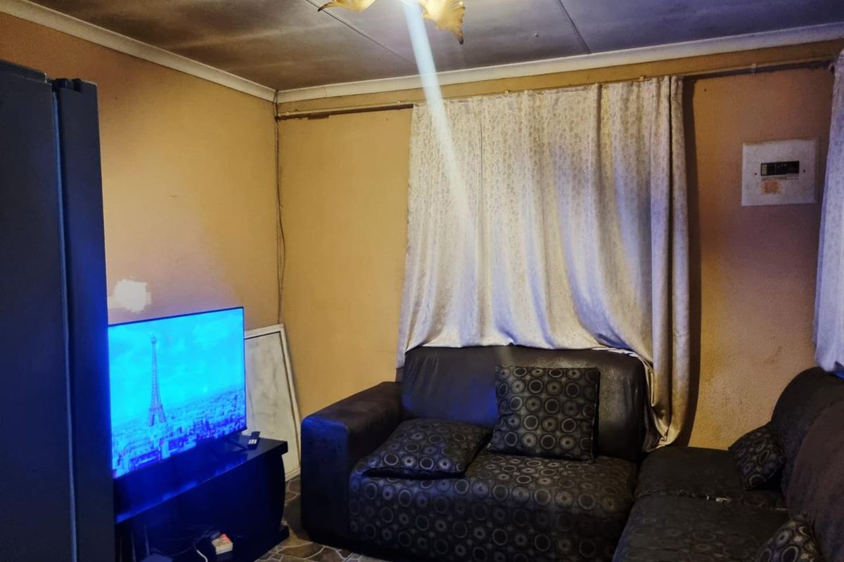 A living room area featuring tiled flooring and an electrical distribution board, currently showing significant signs of wear and ceiling damage.