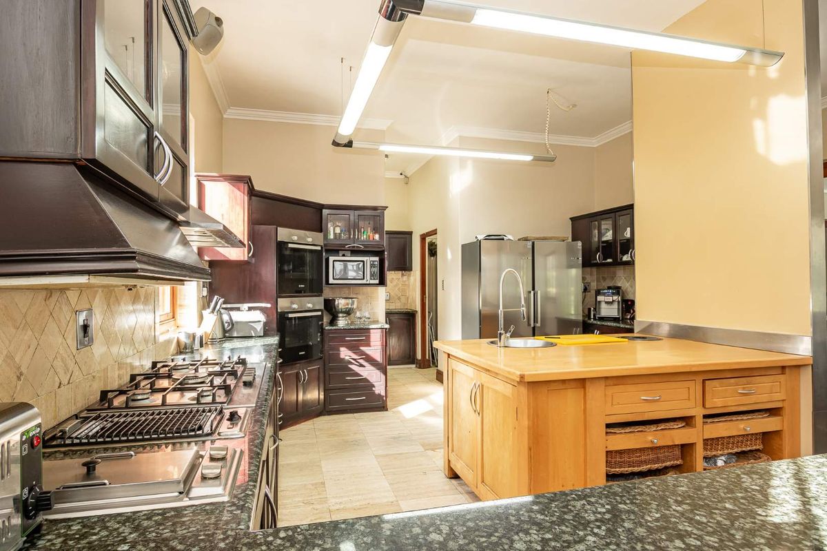 Spacious kitchen featuring dark wood cabinetry, a central wooden island with a prep sink, built-in double ovens, and a gas hob with extractor fan.