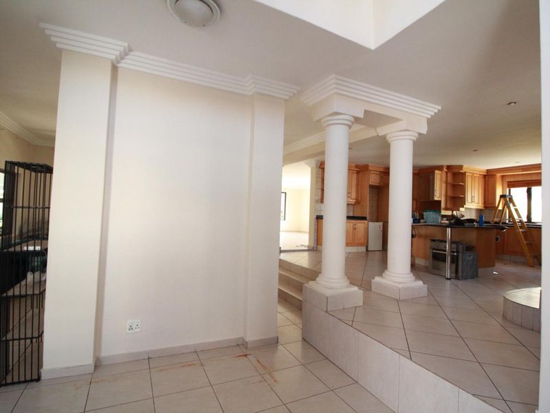 Open plan living area featuring a raised platform with decorative columns, tiled flooring, and a spacious kitchen with wooden cabinetry.