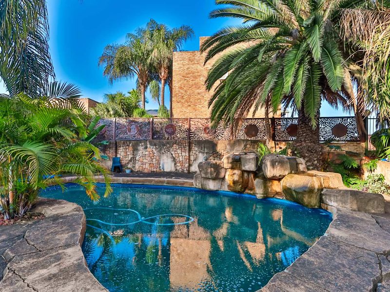 Outdoor pool area featuring a rock water feature, decorative metal privacy screening, and stone walling set within a landscaped garden.