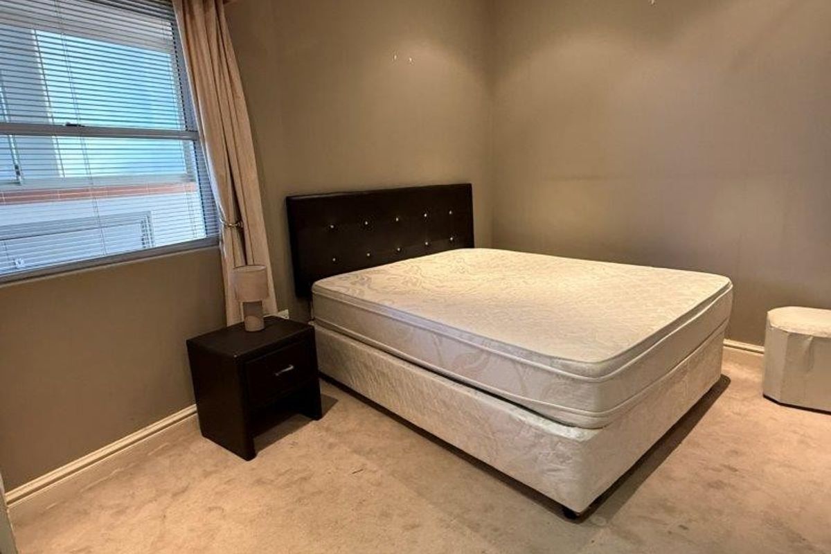 A standard bedroom featuring neutral wall tones, carpeted flooring, and window treatments including venetian blinds and curtains.