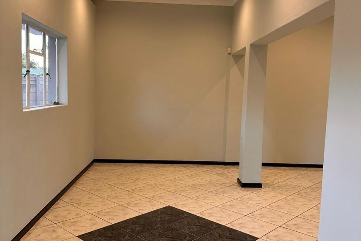 A bright, empty living area featuring neutral walls, tiled flooring with a decorative central inlay, recessed lighting, and an open-plan archway design.