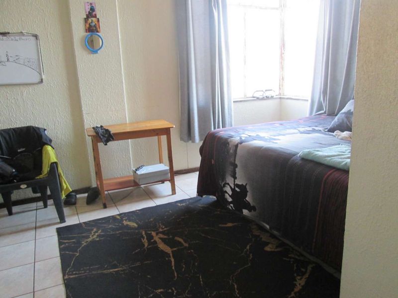 A bedroom featuring tiled flooring and a bay window, requiring cosmetic updates to the wall finishes and window frames.