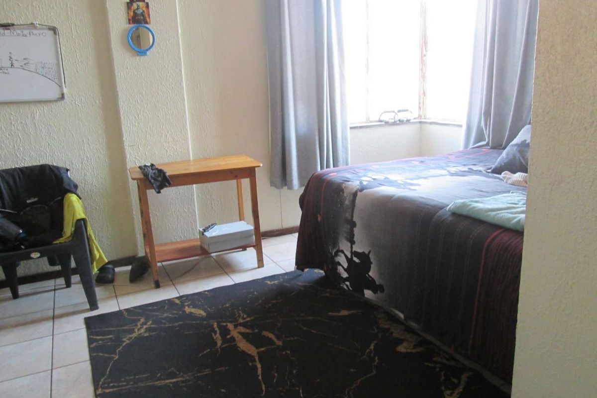 A bedroom featuring tiled flooring and a bay window, requiring cosmetic updates to the wall finishes and window frames.