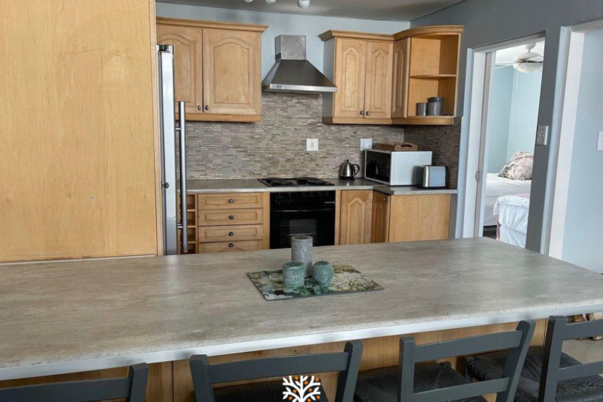 Functional kitchen featuring light wood cabinetry, a stainless steel extractor fan, built-in oven, and a breakfast bar island with stone-look countertop.