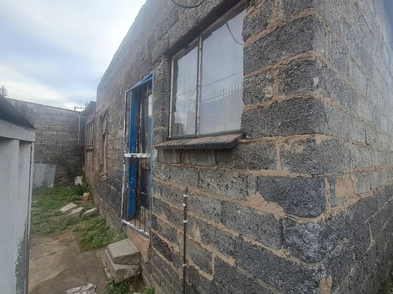 Exterior view of the rear building facade featuring exposed concrete block construction, steel-framed windows, and a metal security gate.