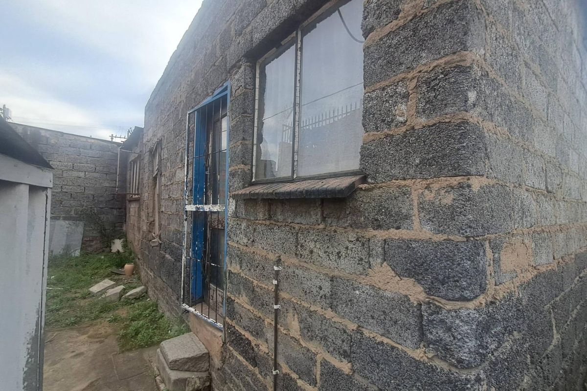 Exterior view of the rear building facade featuring exposed concrete block construction, steel-framed windows, and a metal security gate.