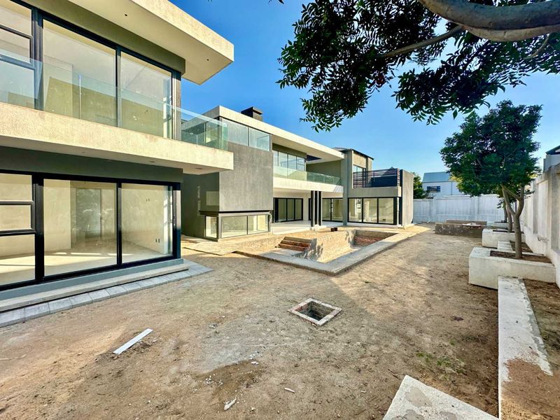 Rear view of a modern multi-level home featuring large sliding glass doors, glass balustrades, and an unfinished swimming pool area with landscaped retaining walls.