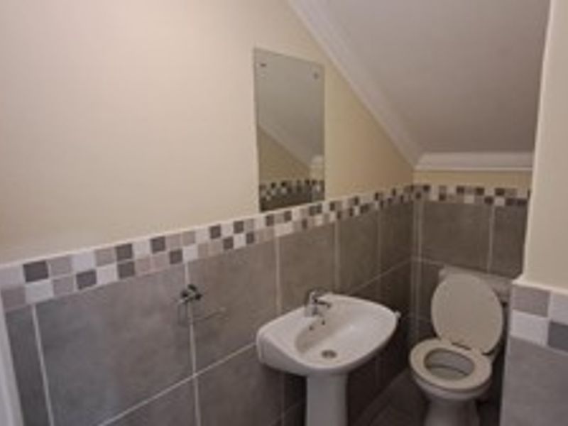 A compact bathroom featuring a pedestal sink, toilet, and neutral wall tiling with a decorative mosaic border.
