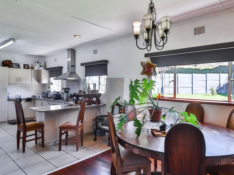 Open-plan kitchen and dining area featuring tiled and timber flooring, granite countertops, a stainless steel extractor fan, and a classic chandelier.