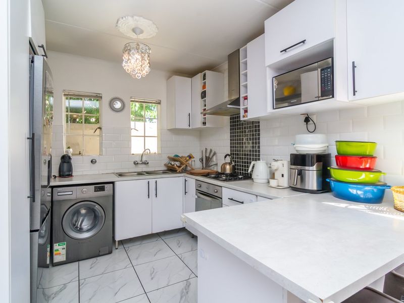 A functional kitchen featuring white cabinetry, subway tile backsplash, built-in oven with gas hob, extractor fan, and integrated microwave, complemented by tiled flooring.
