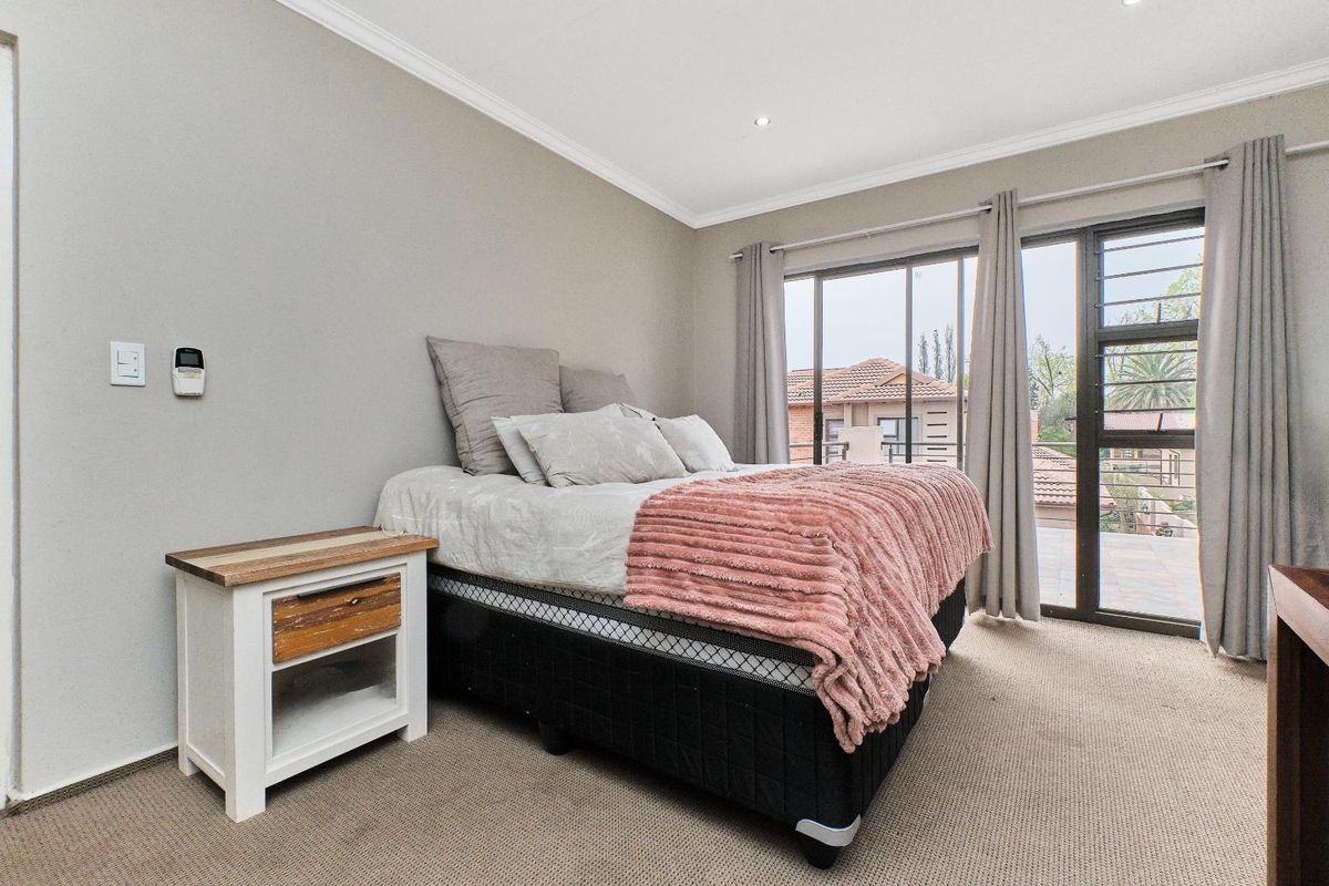 A well-lit bedroom featuring neutral carpeting, recessed ceiling lighting, and sliding glass doors that provide access to an outdoor balcony area.