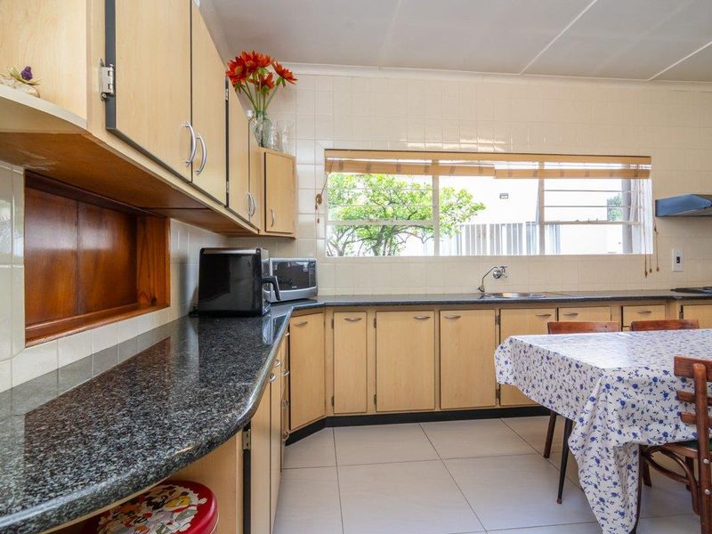 A functional kitchen featuring light wood cabinetry, dark granite countertops, tiled splashbacks, and a built-in extractor fan.