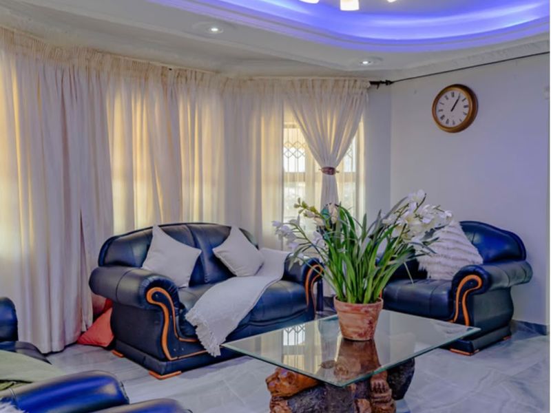 A well-maintained living room featuring decorative ceiling molding with integrated blue cove lighting and polished marble-look floor tiles.