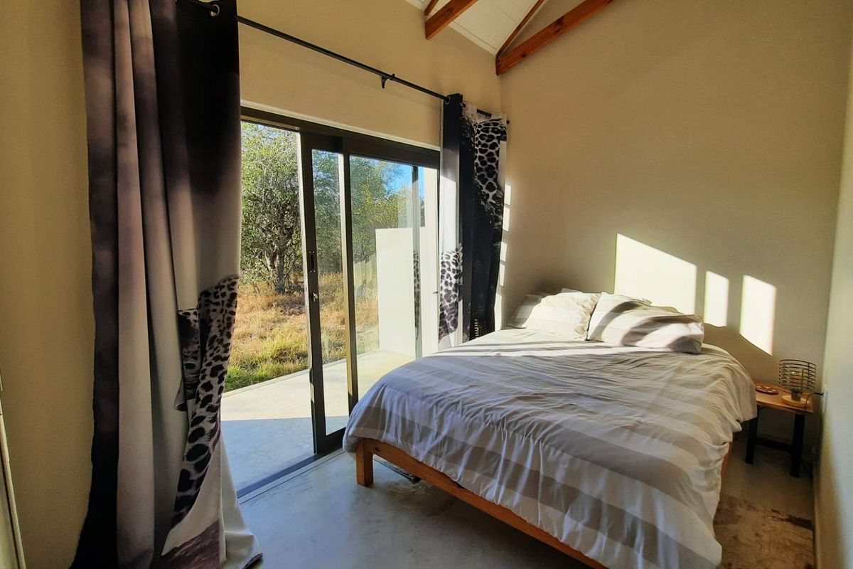 A bright bedroom featuring exposed timber rafters, polished concrete floors, and a large sliding glass door providing direct access to the outdoor area.