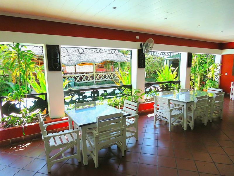 A spacious covered patio area featuring tiled flooring, decorative wrought iron railings, and views of the garden and pool area.