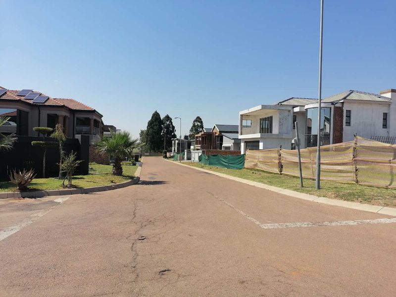 A view of a residential street in a developing estate, featuring paved roads, street lighting, and surrounding residential properties under construction.