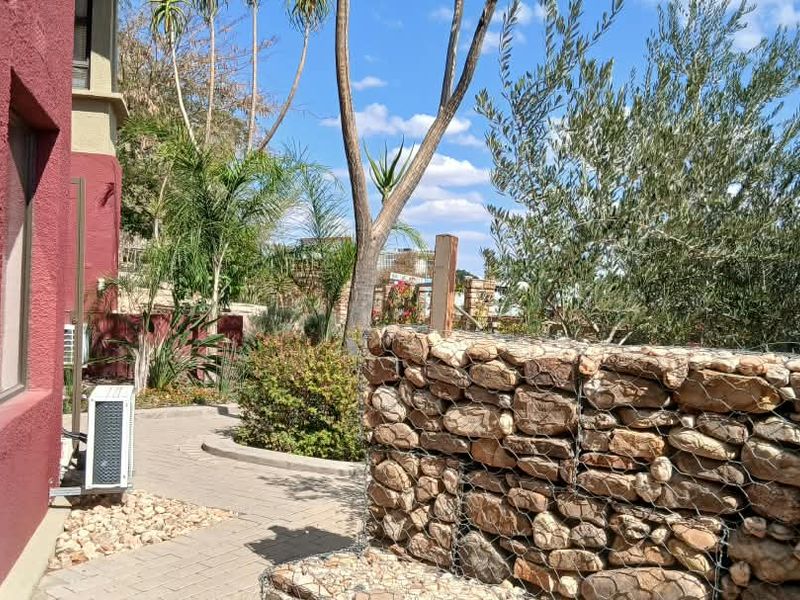 A well-maintained rear exterior area featuring a stone gabion retaining wall, paved pathway, and established garden landscaping alongside the office building.