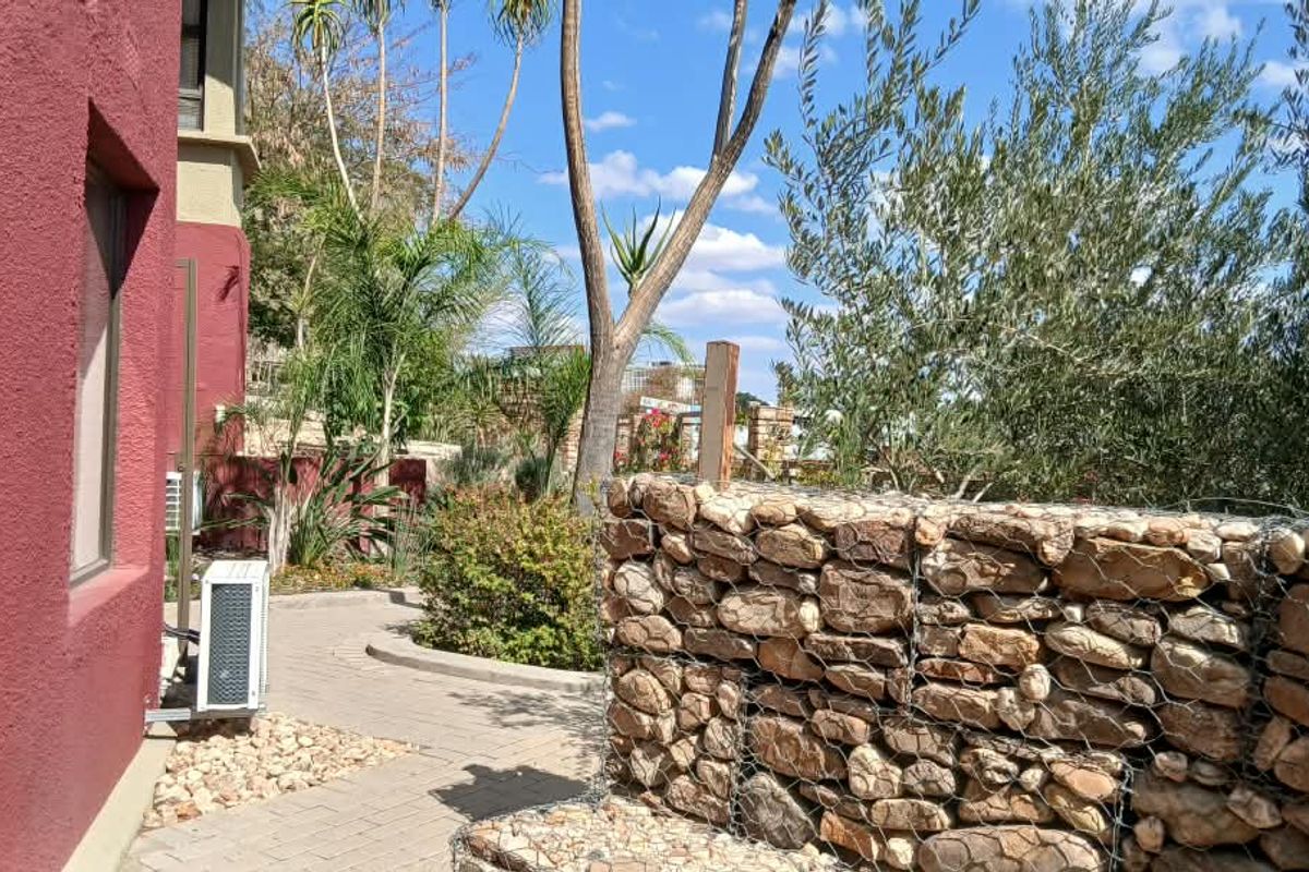 A well-maintained rear exterior area featuring a stone gabion retaining wall, paved pathway, and established garden landscaping alongside the office building.