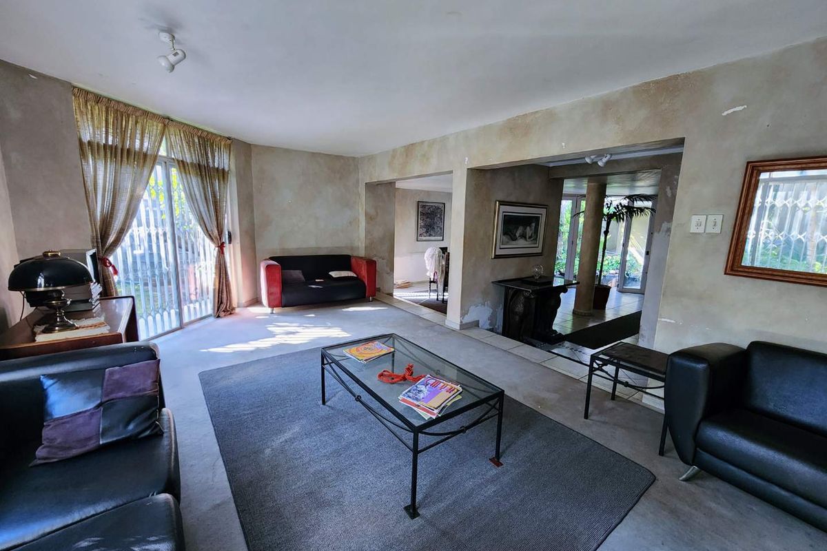 Spacious living area featuring large sliding glass doors with security gates, neutral tiled flooring, and walls requiring cosmetic attention and fresh paint.