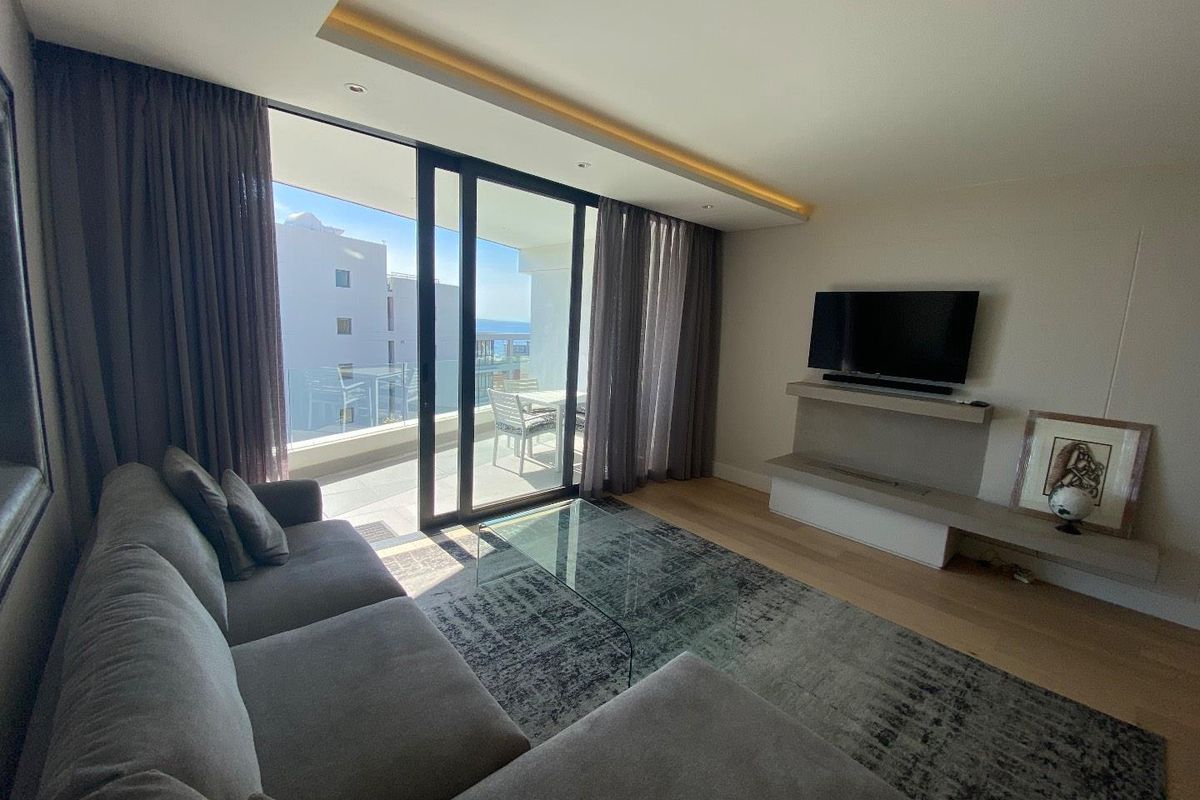 Modern living room featuring hardwood flooring, recessed ceiling lighting, and large sliding glass doors opening onto a private balcony with exterior views.