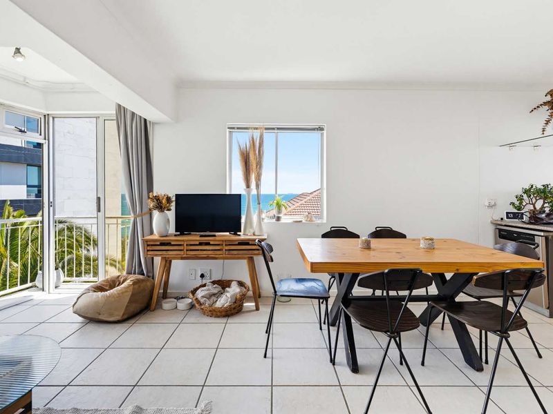 Open plan living and dining area featuring tiled floors, neutral walls, and direct access to a balcony with ocean views.