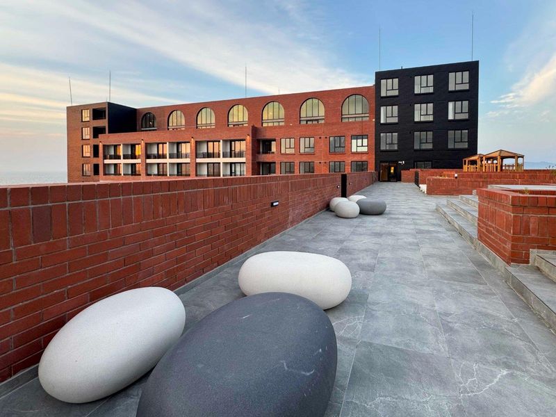 A spacious outdoor terrace featuring modern tiled flooring, brick architectural elements, and a clear view of the apartment building facade.