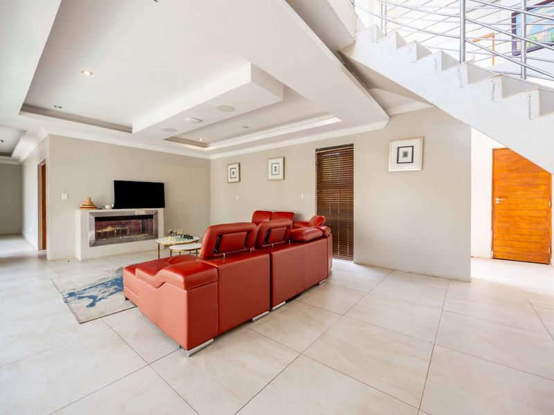 Spacious living room featuring a modern built-in fireplace, recessed ceiling lighting, and a contemporary staircase with a metal balustrade, finished with neutral floor tiles.