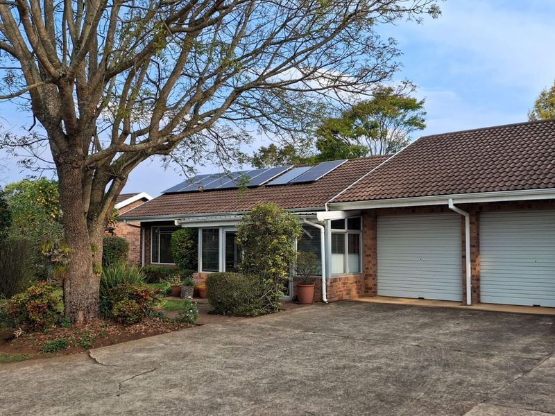 Front exterior view of a townhouse featuring a double garage, brick facade, tiled roof, and installed solar panels with a mature garden.