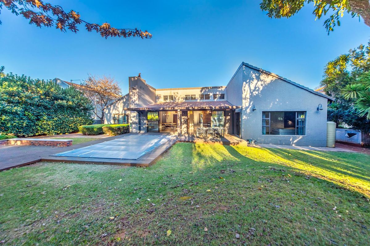 Rear view of the property featuring a spacious garden, a wooden deck with a swimming pool cover, and a covered patio area.
