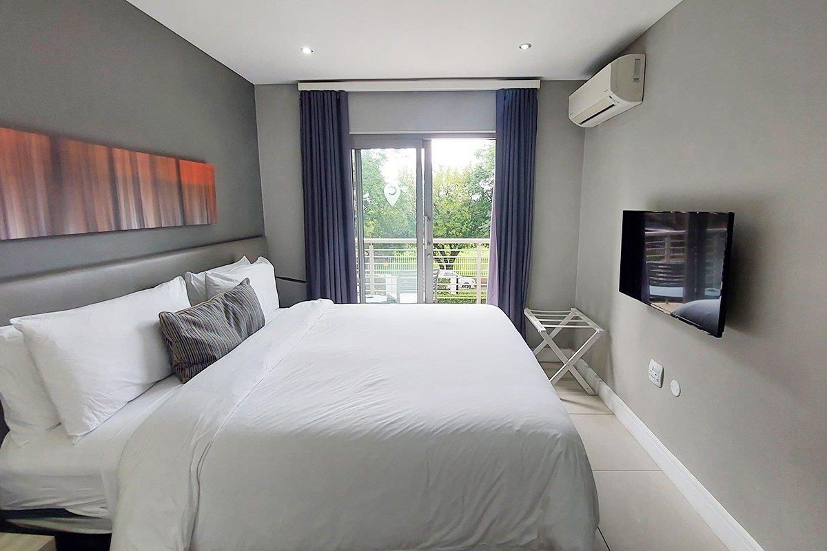 A well-maintained bedroom featuring tiled flooring, recessed lighting, a wall-mounted air conditioning unit, and a sliding glass door leading to a balcony.