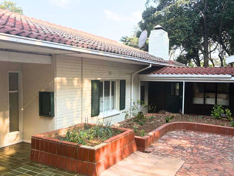Rear exterior view featuring a brick paved patio, raised planter beds, and a classic tiled roof with a prominent brick chimney.
